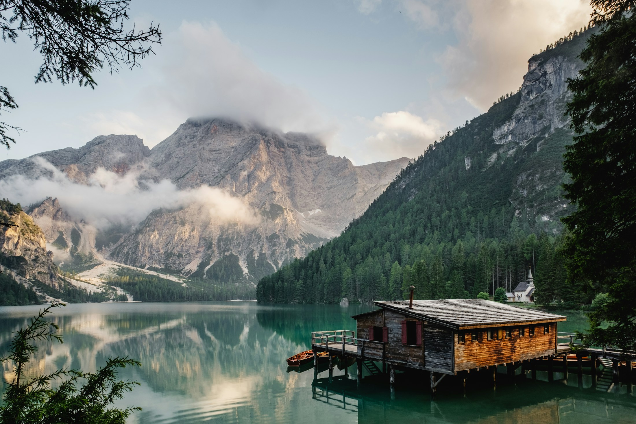A timber house at the edge of a still alpine lake beneath forested mountains